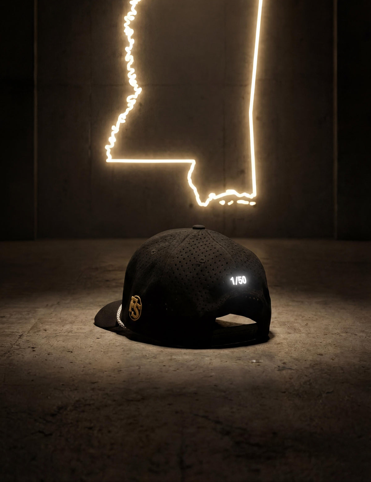 Neon outline of the state of Alabama on a dark wall with a cap in the foreground.