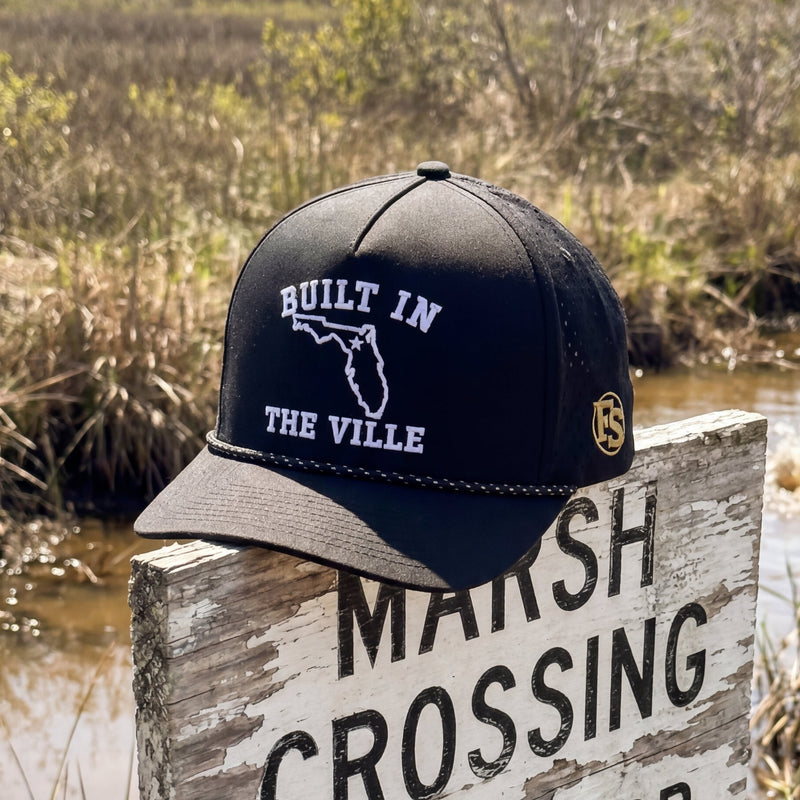 Cap with 'Built in the Vile' text on a marsh crossing sign with wildlife warning.