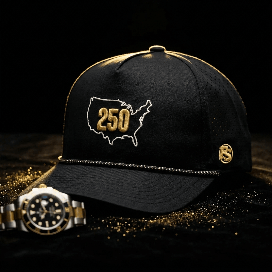 USA 250 on a dark table beside a watch, with a white US outline, gold 250, gold FS badge and perforated panels.